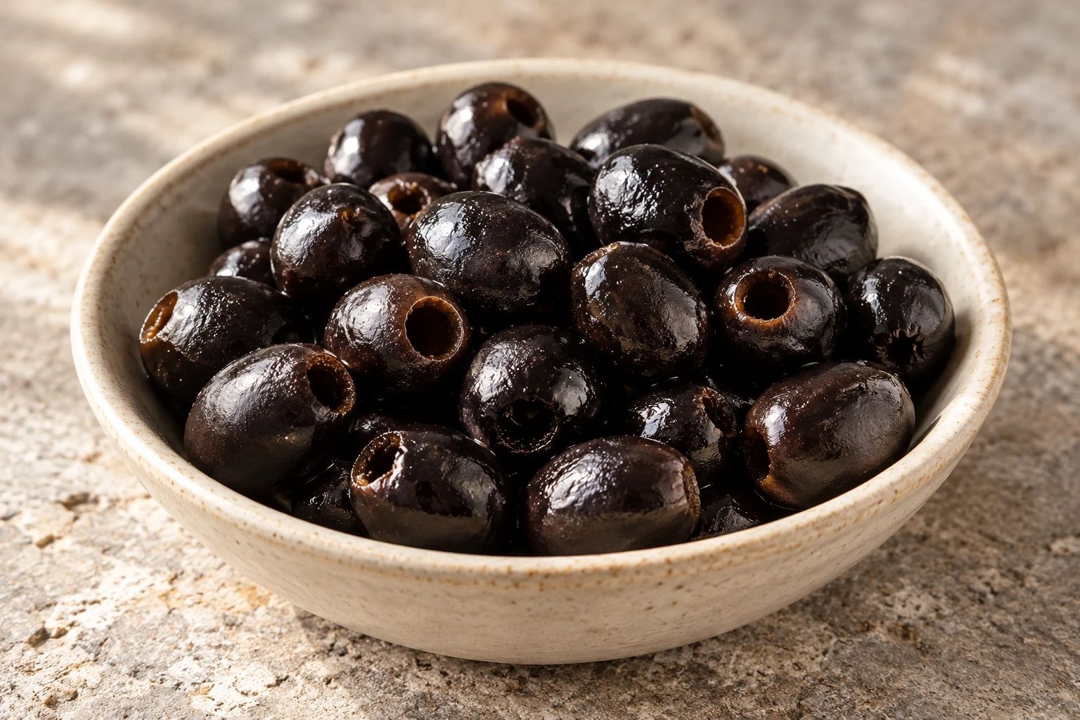 Pitted black olives with moist irregular skins in a shallow ceramic bowl.