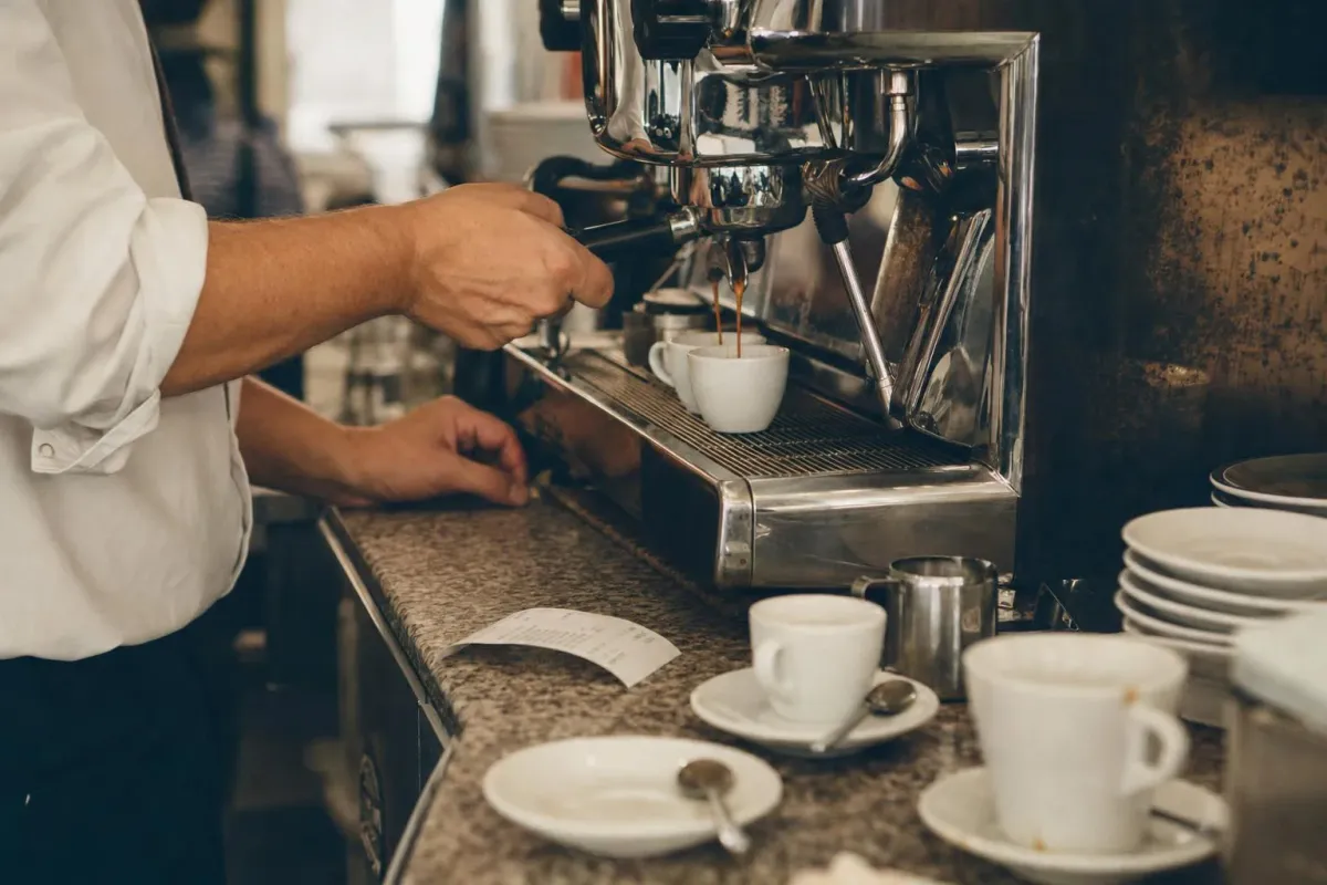 A barista pulling an espresso at the counter of a busy Italian bar
