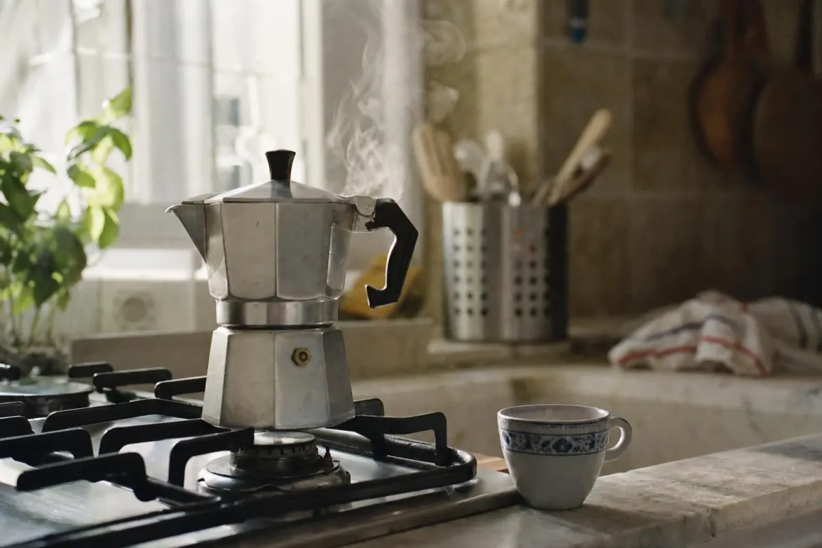 A classic octagonal aluminium moka pot on a stovetop with steam rising
