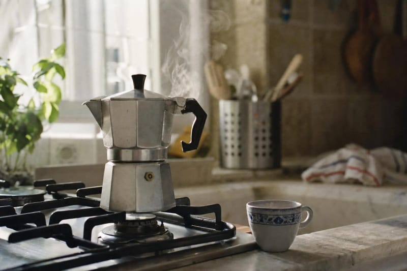A classic octagonal aluminium moka pot on a stovetop with steam rising