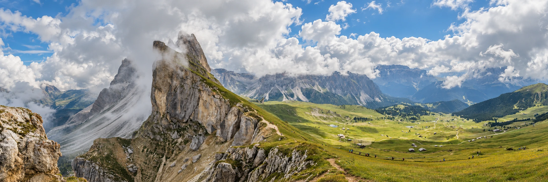 Cloud-veiled rock faces beside a grassy ridge and paths at Seceda