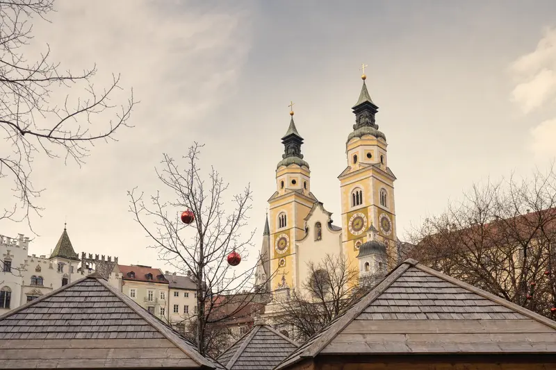 Wooden Christmas-market roofs and red baubles beneath Bressanone Cathedral’s twin towers