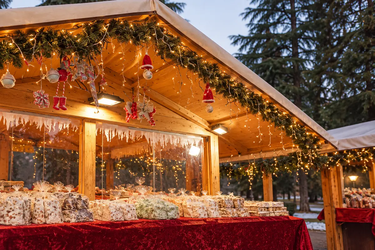 Wrapped sweets on a red counter beneath a garlanded wooden chalet in Levico Terme’s Habsburg park