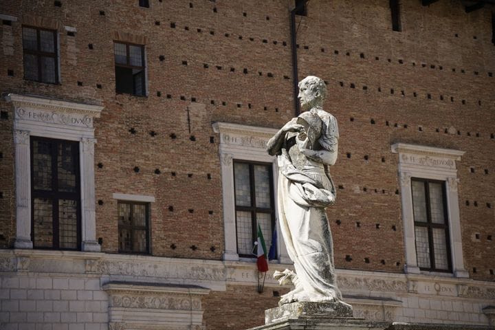A statue before the brick facade of the Palazzo Ducale, Urbino