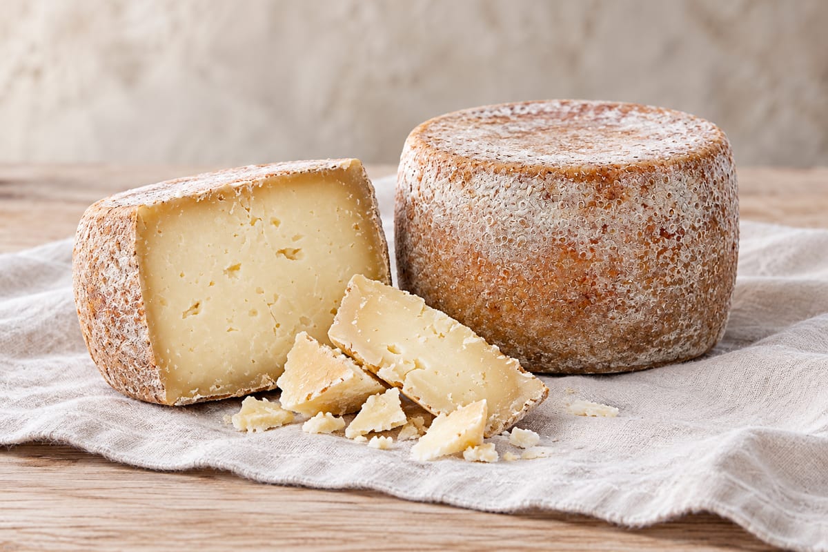 An aged wheel of Pecorino Toscano with a golden rind beside a cut half and broken flakes
