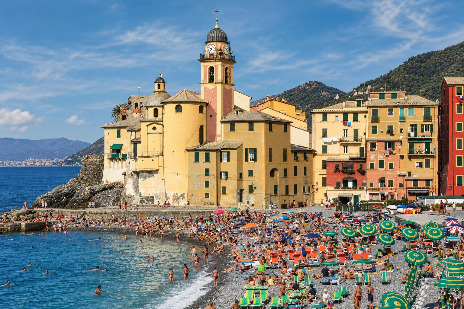 Camogli’s pebble beach, with the yellow and pink basilica, waterfront houses, umbrellas and the sea.