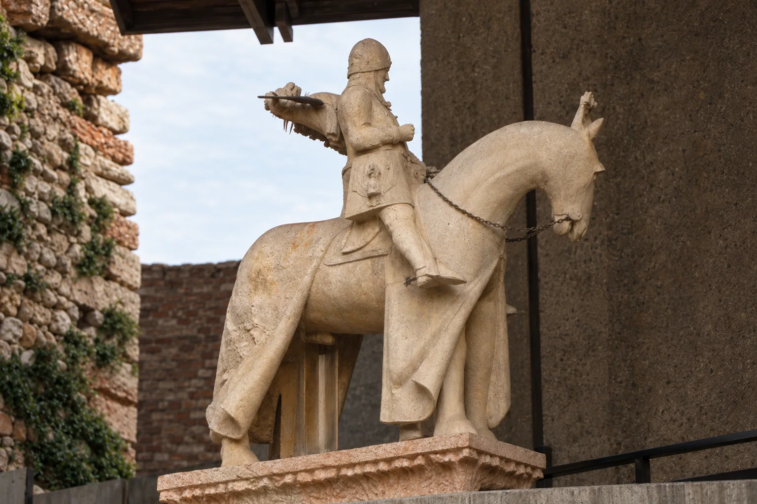 Pale stone horse and armoured rider, with horse facing right and the rider’s extended arm pointing left, on a plinth above a concrete support.