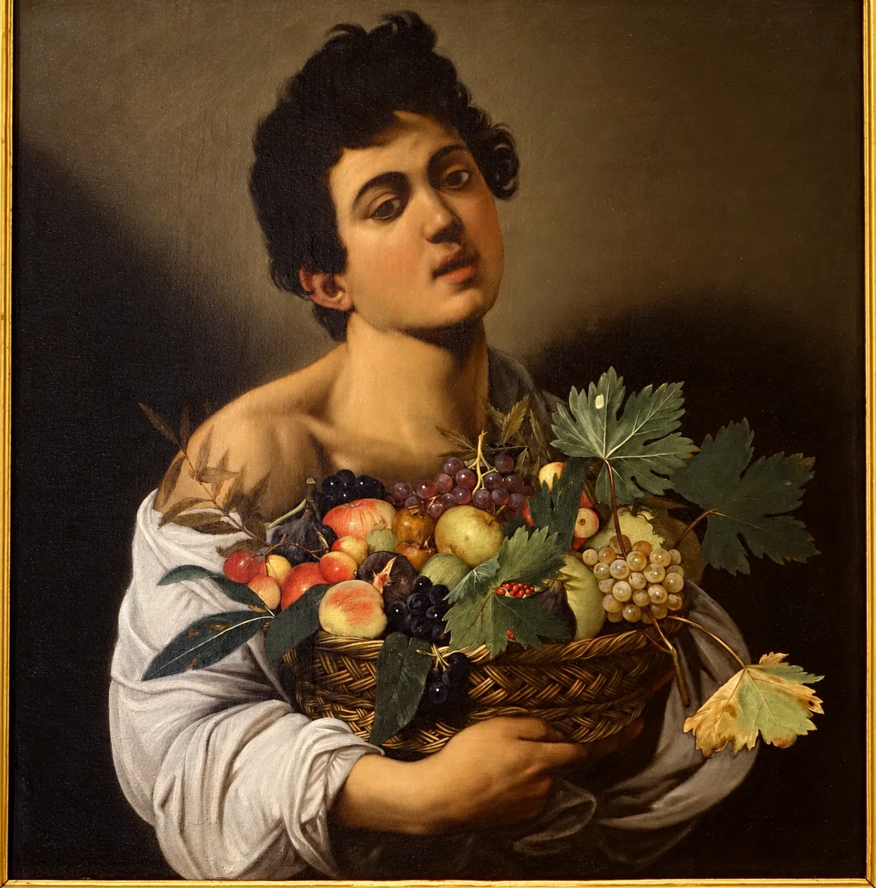 Detail of Caravaggio’s painted young man holding a fruit basket inside a gilded frame