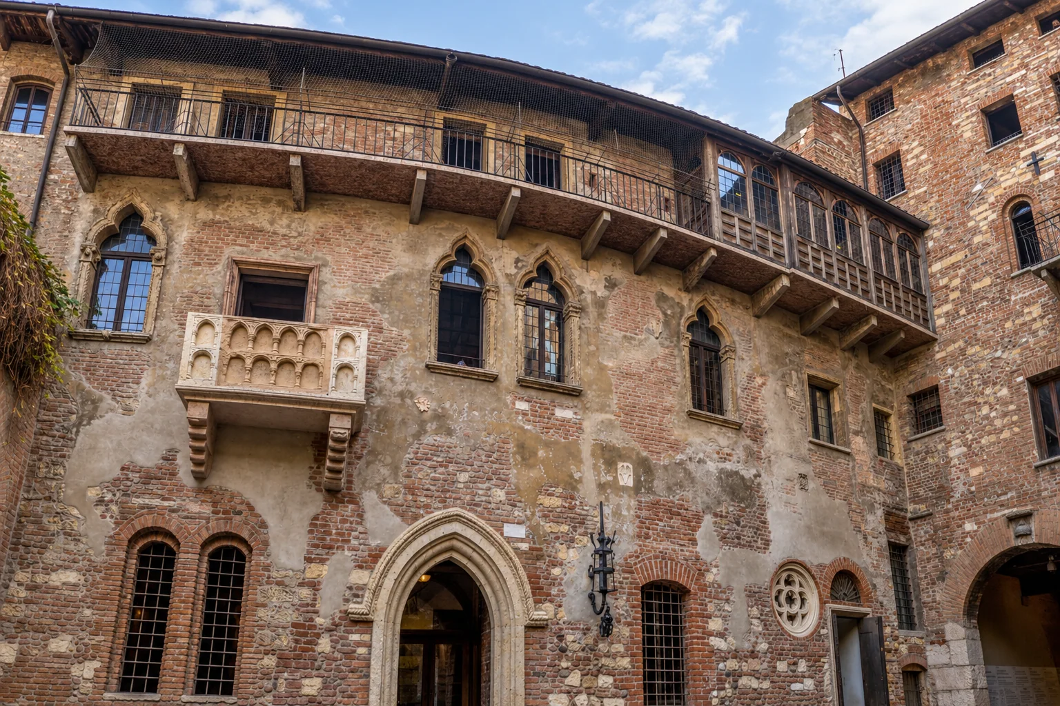Courtyard façade with a projecting stone balcony, pointed windows, upper wooden gallery and large pointed doorway.