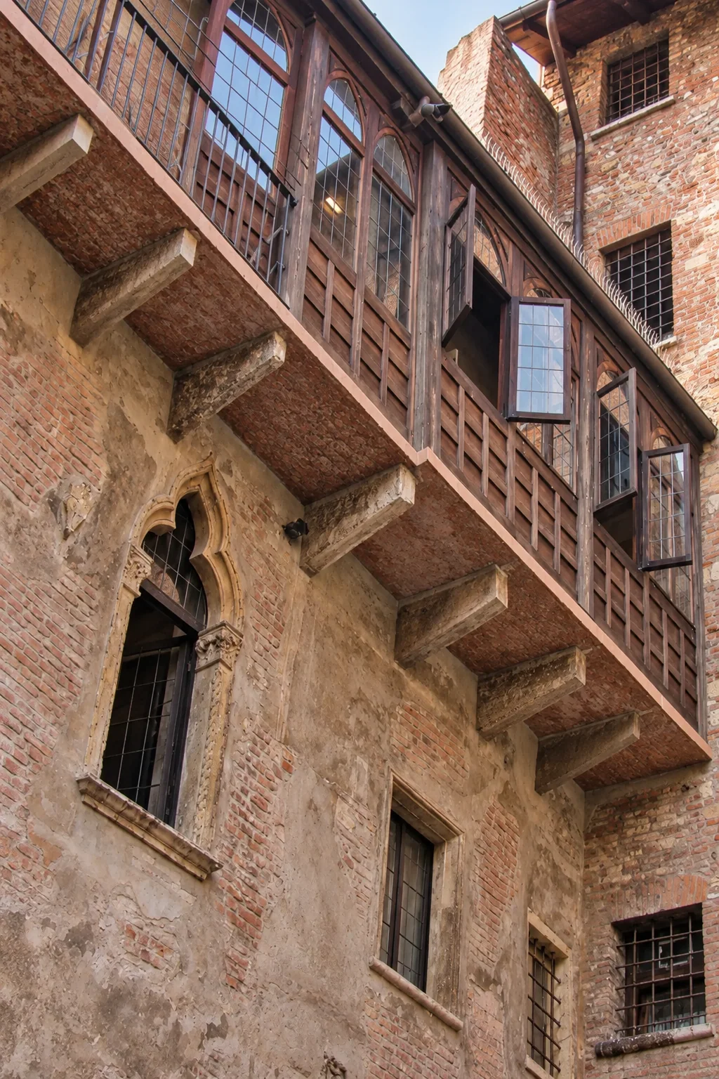 Upward view of the courtyard’s timber-framed gallery, glazed panels, projecting stone supports and trefoil-shaped window below.