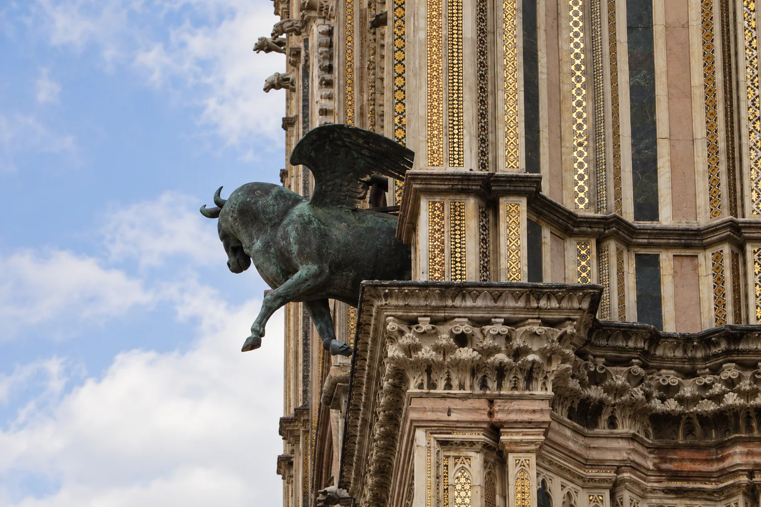 Green-patinated projecting bronze beside narrow vertical mosaic bands and a carved stone cornice.