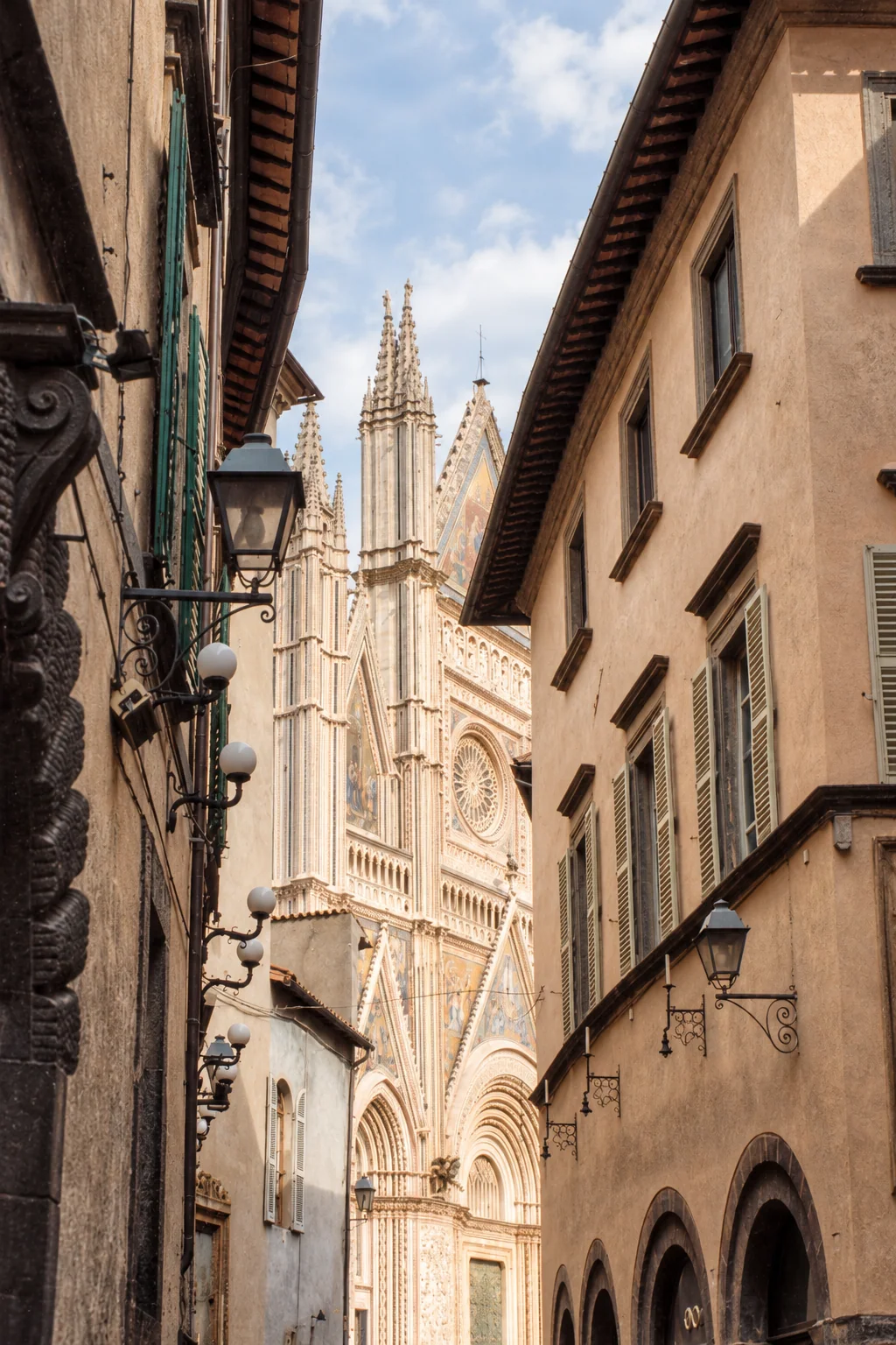 Partial oblique view of Orvieto Cathedral’s spires and façade, framed by the roofs and windowed walls of a narrow street.