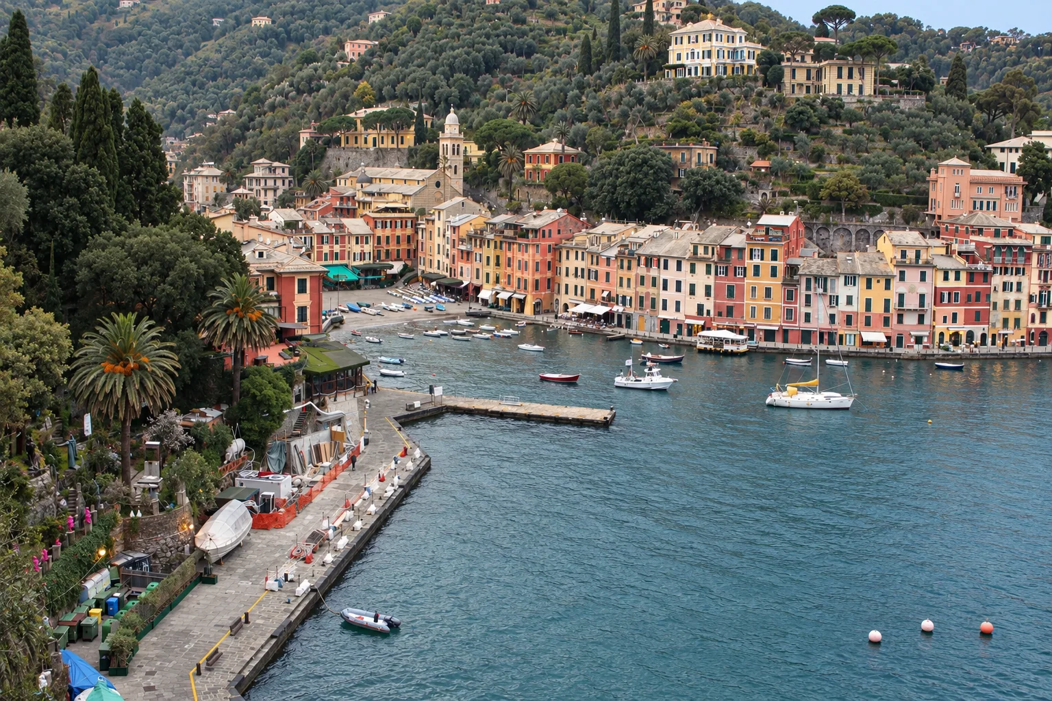 Sopra il porto di Portofino: Una veduta dall’alto sul bacino interno di Portofino, la banchina vicina e le facciate color pastello sotto la collina boscosa.