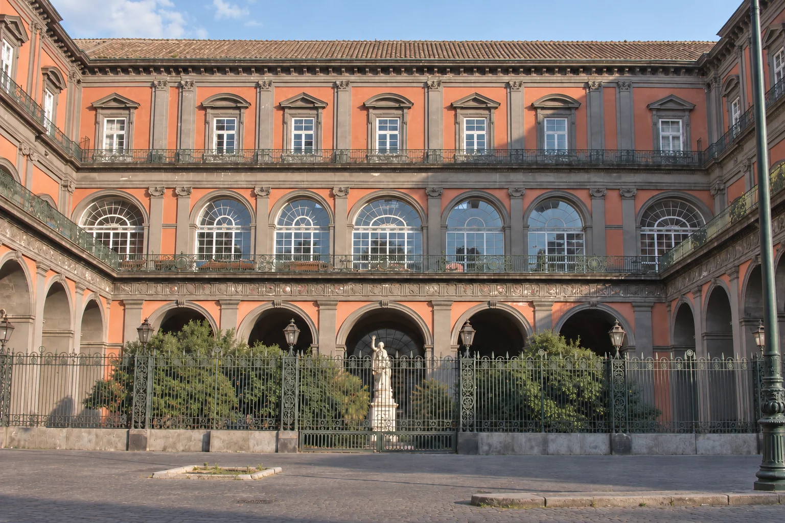 The side courtyard on the Galleria Umberto I side, with an arcade below upper arched windows and a small garden sculpture.