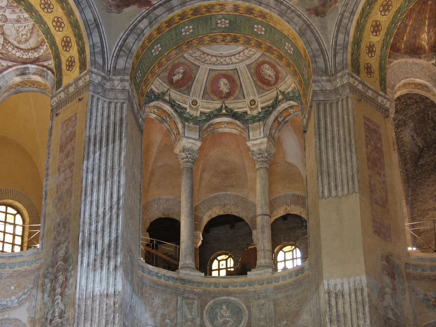 Upper round arcades and curved gallery parapet between two marble-faced piers inside San Vitale.