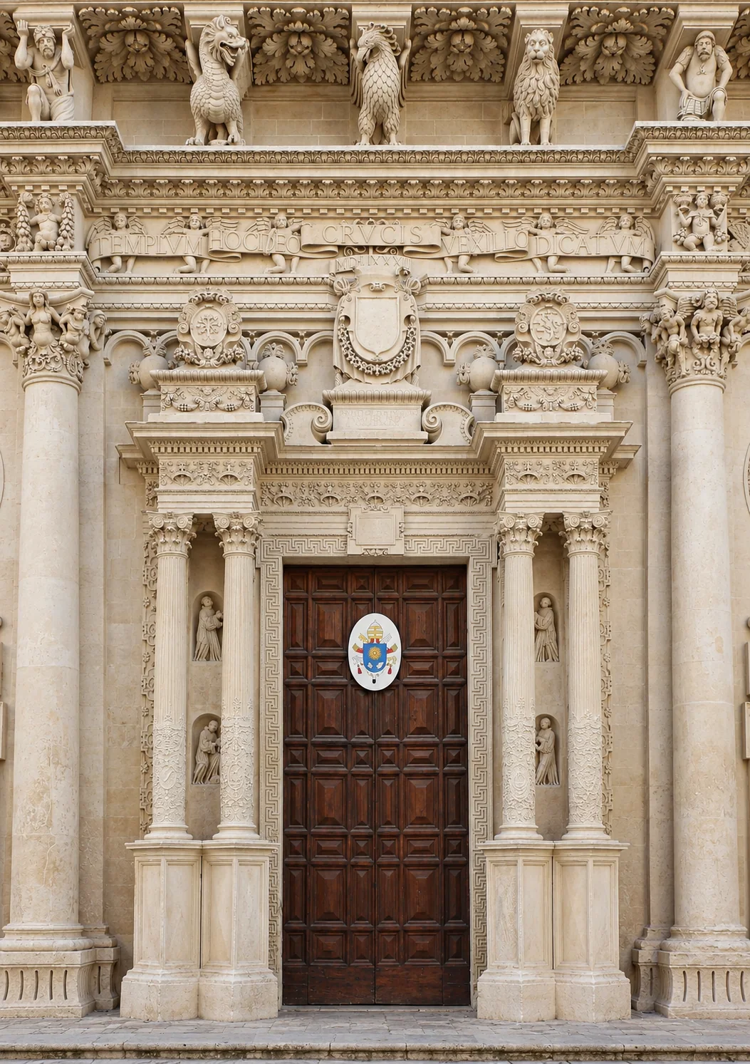 Dark paneled entrance door within a carved Greek-key surround, four small niche figures and paired columns beneath stone urns and shields.