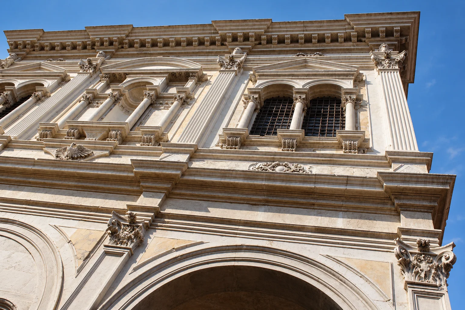 Low-angle detail of pale stone columns and pedimented openings above a large entrance arch at Scuola Grande di San Rocco.
