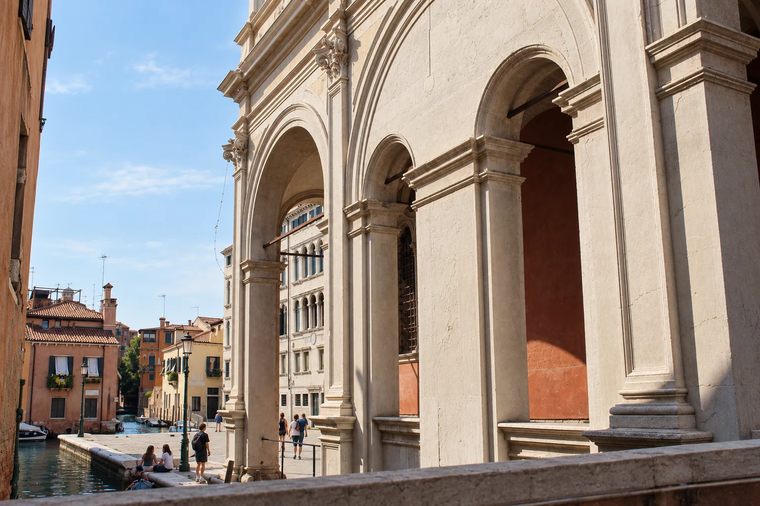 Oblique view of a pale stone arcade with broad outer arches and smaller openings, with a canal and Venetian houses at left.