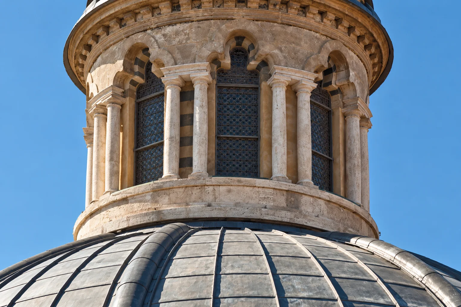 Pietra e metallo sopra il Duomo: La parte inferiore della lanterna e la copertura metallica curva della cupola del Duomo di Siena, in un dettaglio architettonico.
