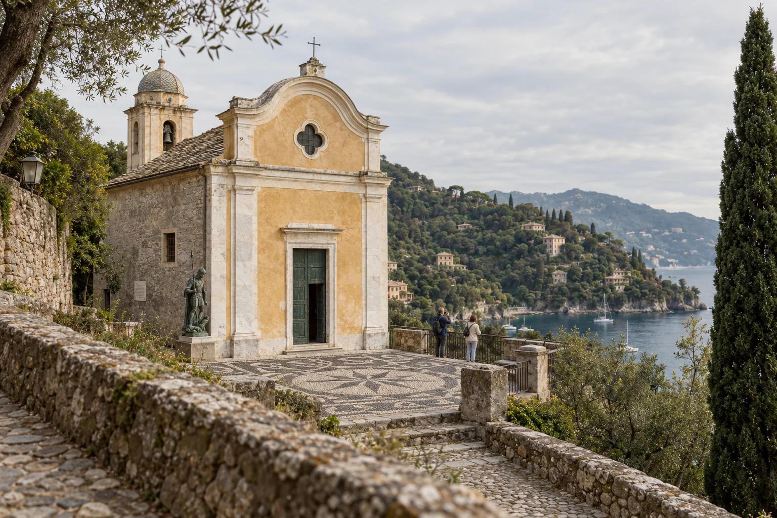 The church of San Giorgio above Portofino with its ochre facade and a pebble mosaic forecourt, visitors at the railing