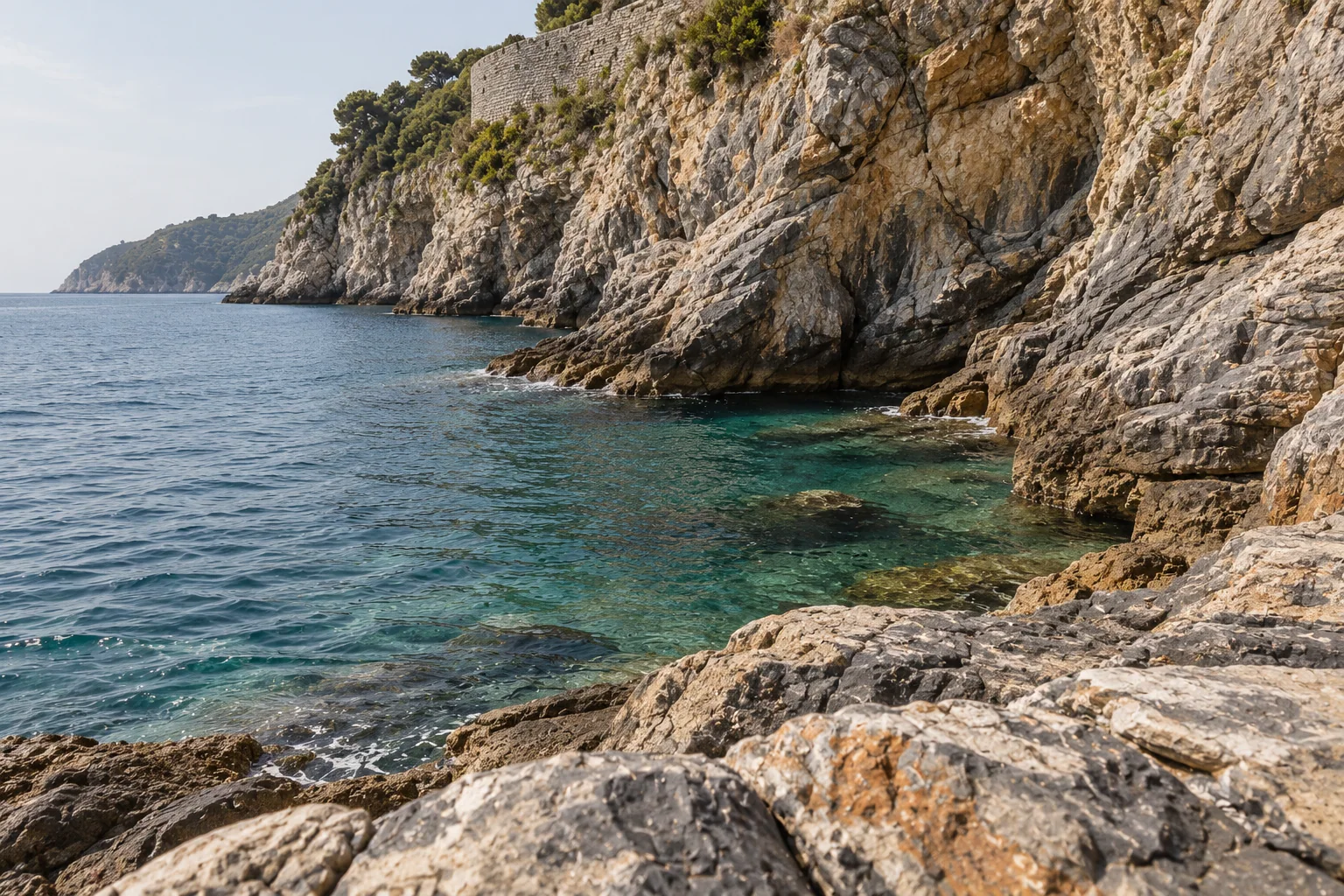 The rocky cliffs and deep blue water below San Pietro at Portovenere, with the castle above