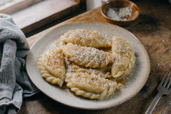 Cjarsons on a pale plate, crimped half-moon dumplings glossy with butter under grated smoked ricotta and a dusting of cinnamon.