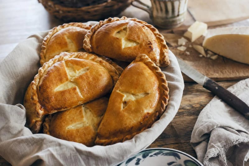 Fiadoni piled in a cloth-lined basket, golden egg-glazed half-moons with cheese peeking through their cross vents, a wedge of pecorino behind.